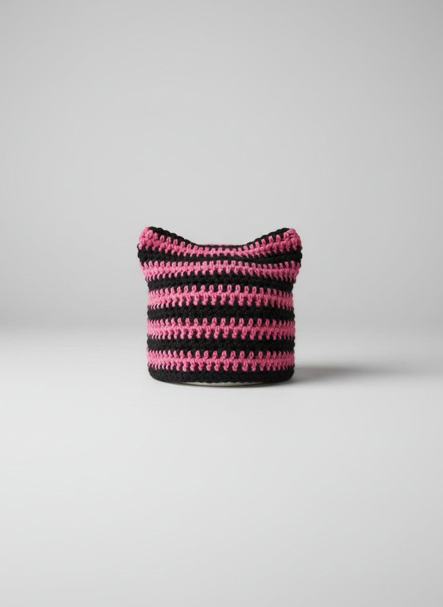 Crocheted cat ear hat with pink and black stripes on a gray background