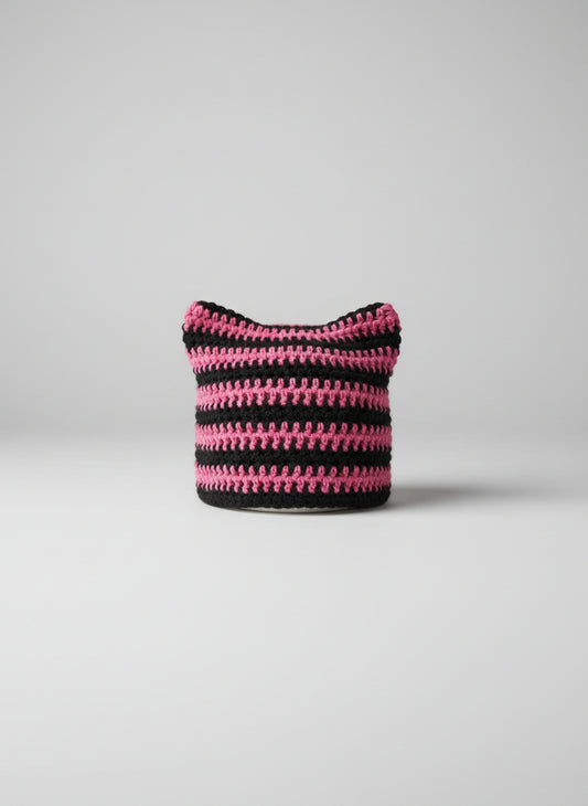 Crocheted cat ear hat with pink and black stripes on a gray background
