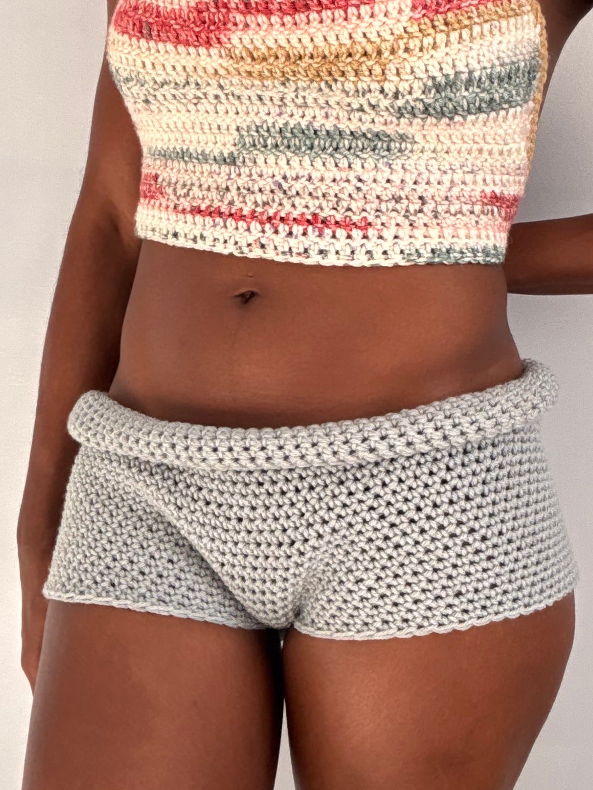 Person wearing a patterned crochet top and shorts on a plain background
